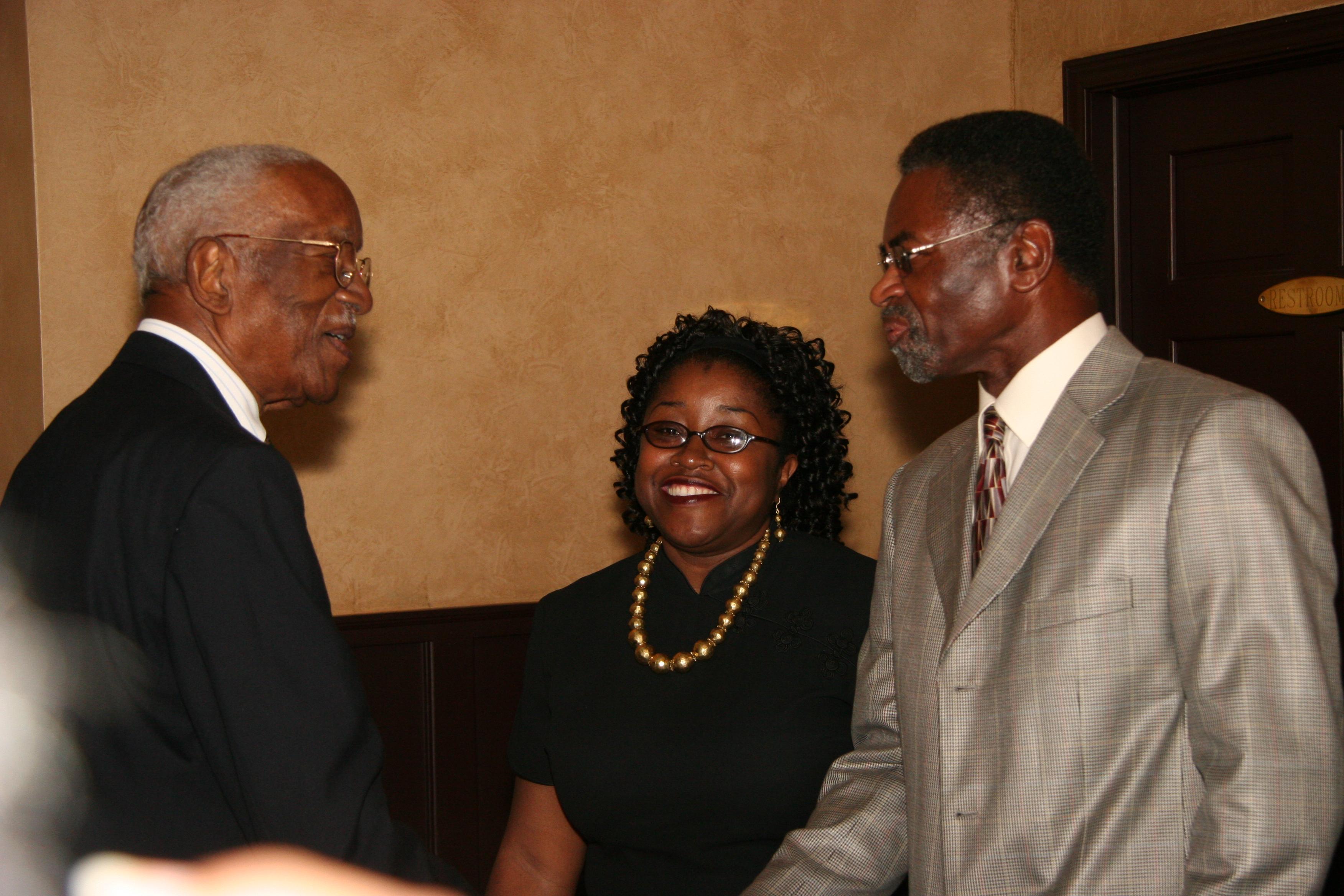 Two men shaking hands with a woman in the background