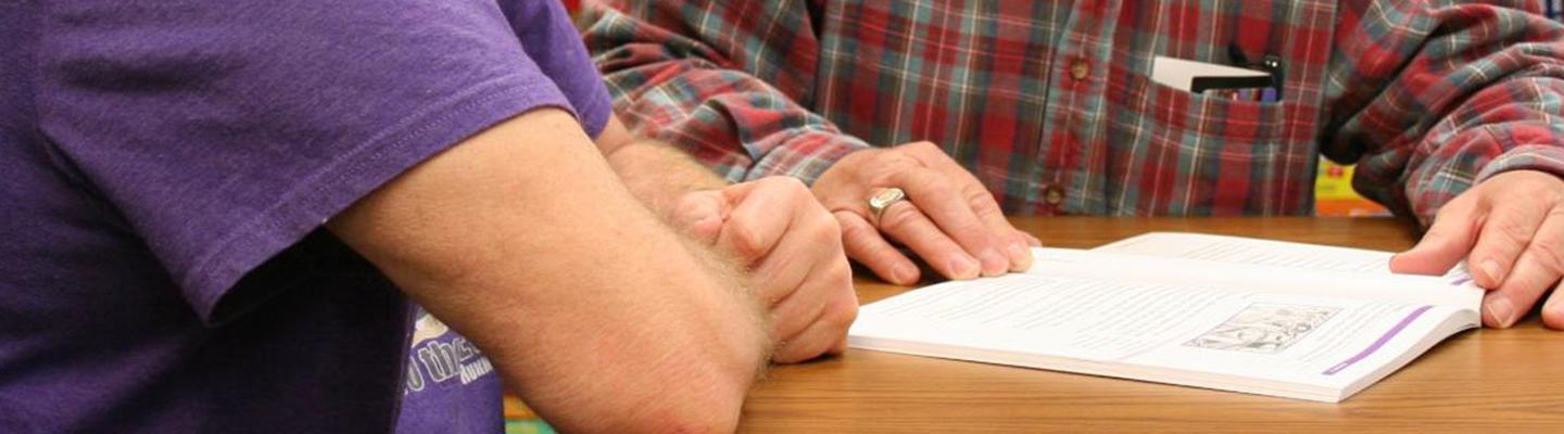 Two adult men study a workbook together